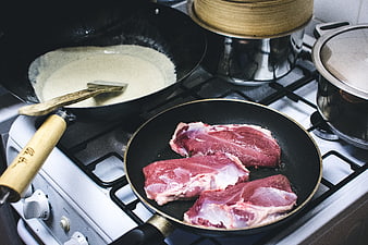 Raw duck breasts frying in pan on gas stove