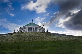 White Pavilion on Grassy Dune Under Dramatic Cloudy Sky