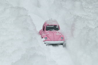 Pink toy Volkswagen Beetle buried in deep winter snow