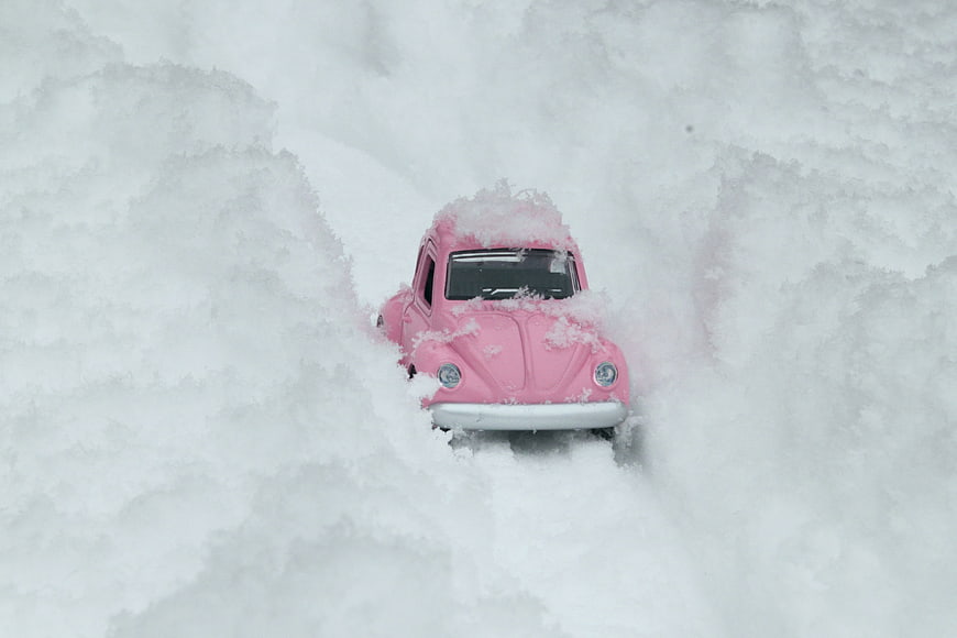 Pink toy Volkswagen Beetle buried in deep winter snow