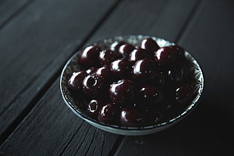 Dark cherries in a patterned bowl on black wood