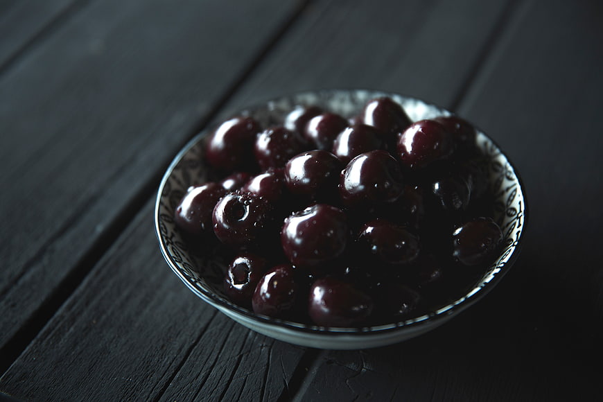 Dark cherries in a patterned bowl on black wood