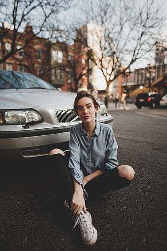 Young woman sitting on street tying shoelaces near car