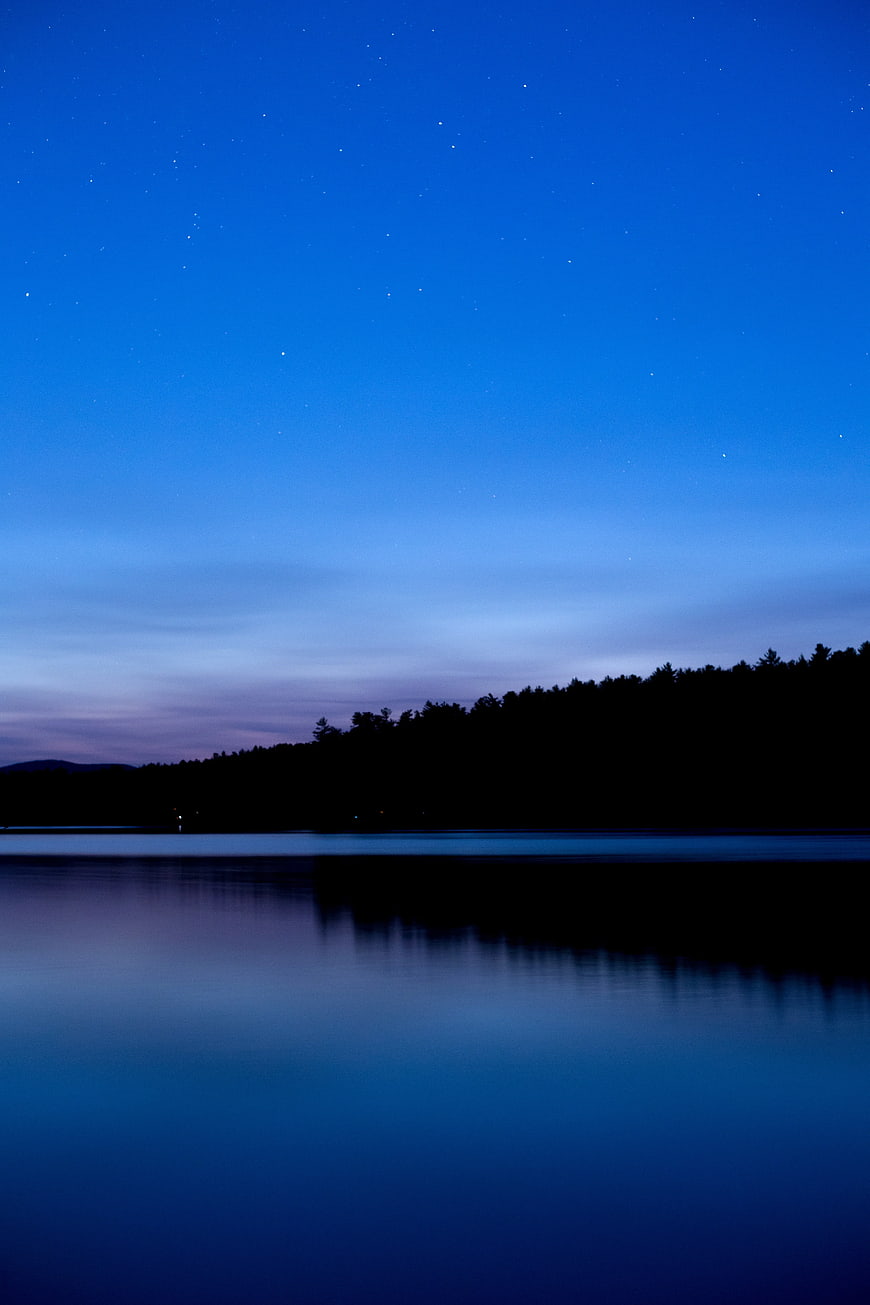 Serene Night Sky Over Calm Lake With Forest Silhouette