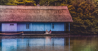 Two women relaxing on a dock by a blue lakeside cottage