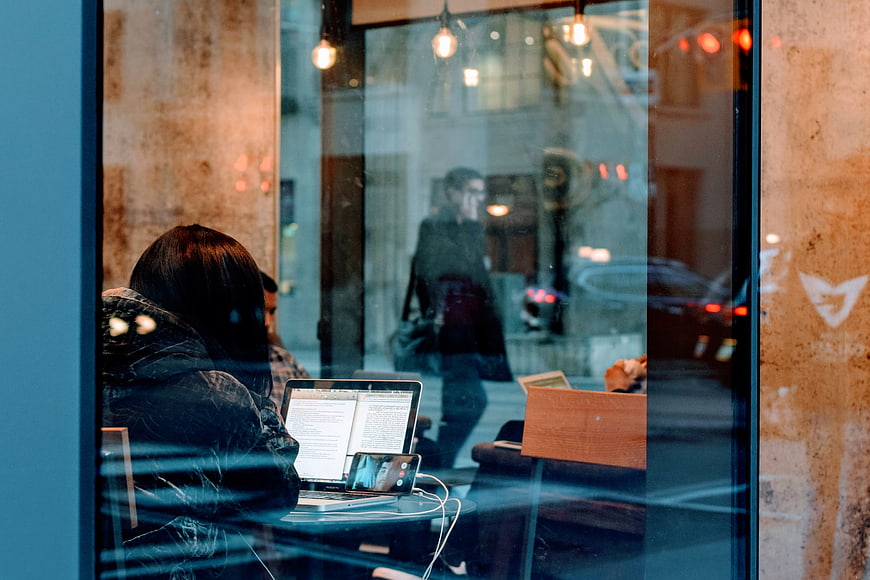 Woman working on laptop in cafe window with street reflection