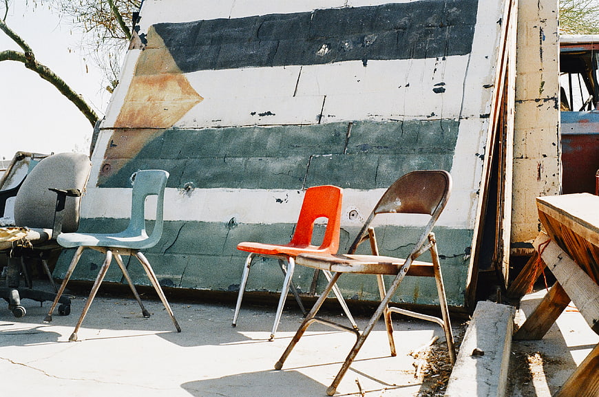 Rusty chairs in front of a weathered wall with a painted flag