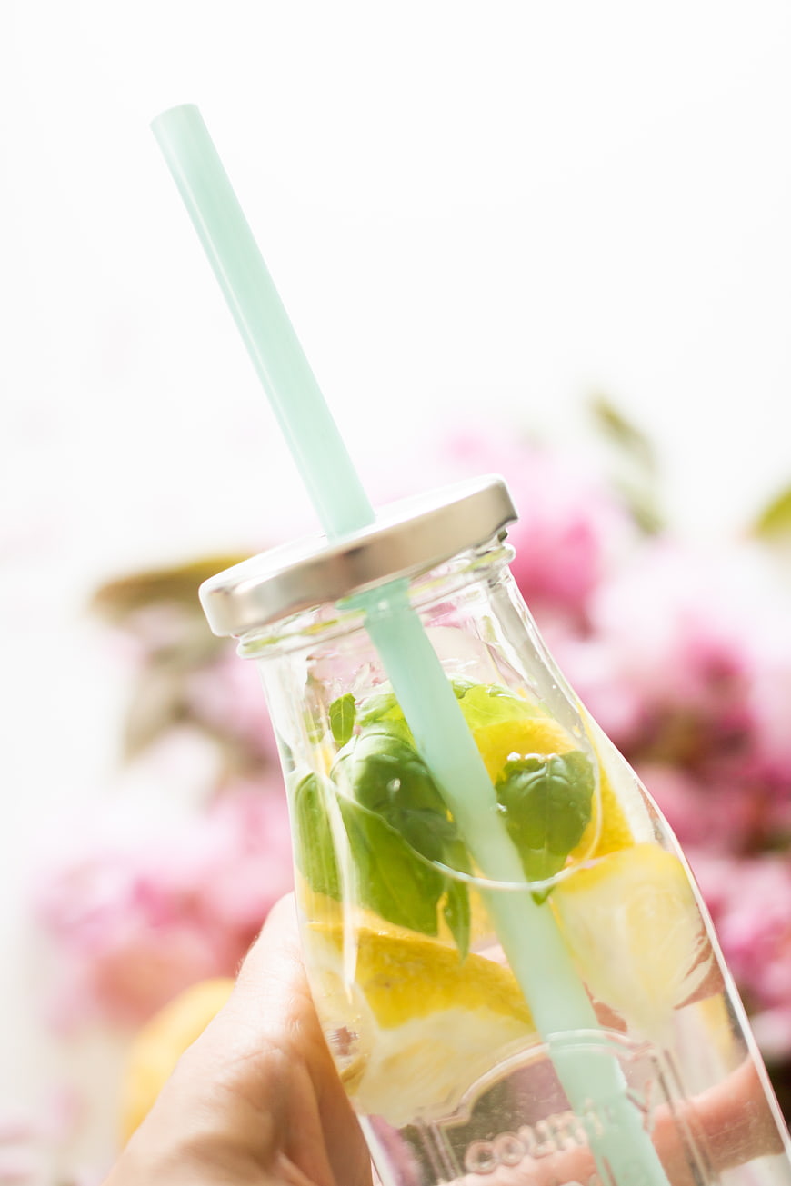 Hand holding glass bottle of lemon mint water with straw