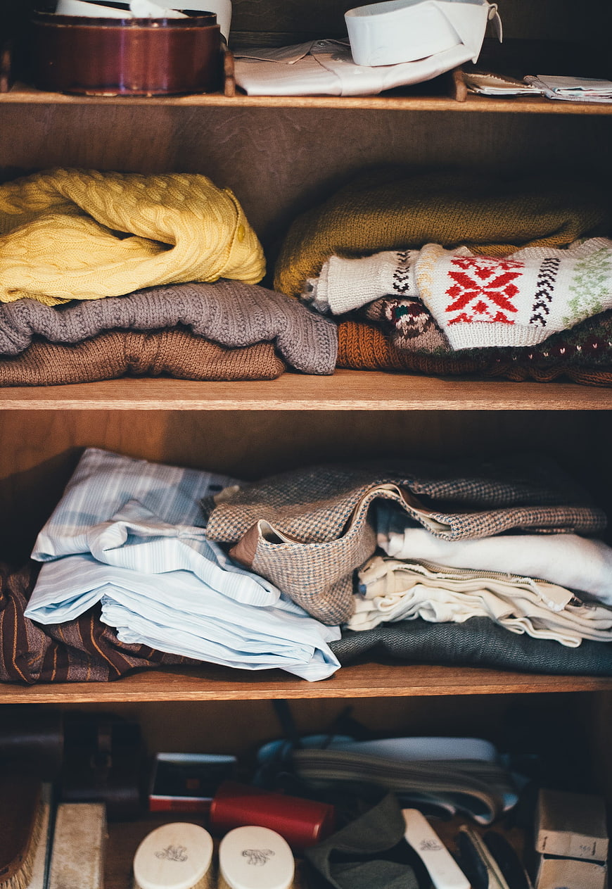 Organized wooden wardrobe shelves with folded knitwear and shirts