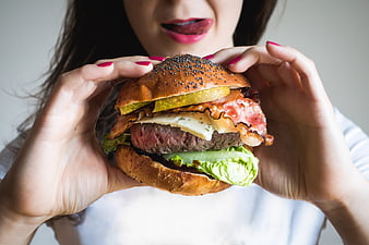 Woman holding large gourmet burger with bacon and cheese