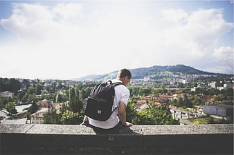Young man with backpack sitting on ledge overlooking city