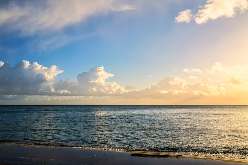 Serene Ocean Sunset with Golden Sky and Fluffy Clouds