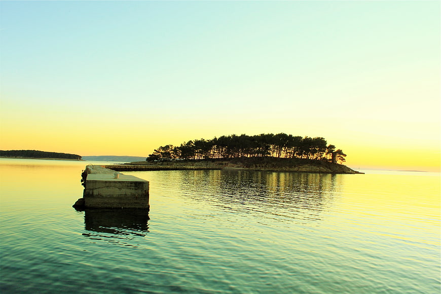Serene Sunset Over Small Forested Island with Concrete Pier