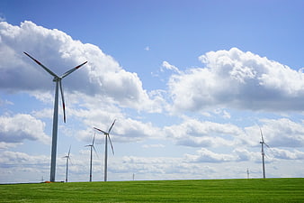 Wind turbines on green field under blue sky with clouds