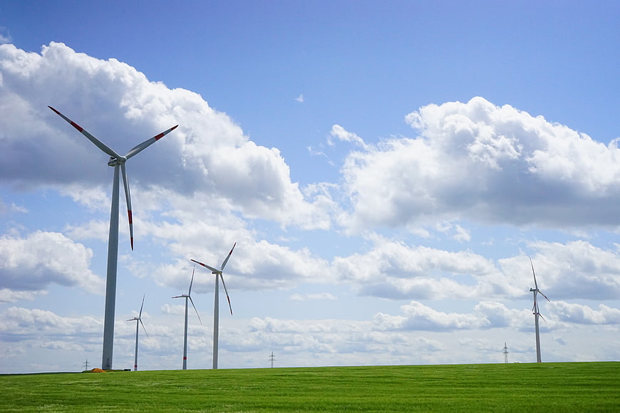 Wind turbines on green field under blue sky with clouds
