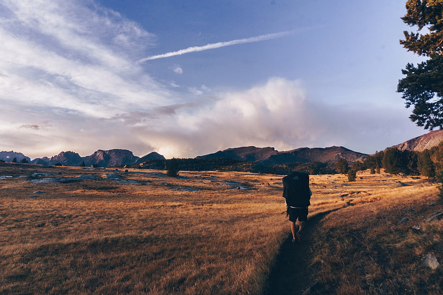 Hiker with backpack walking on mountain trail at sunset