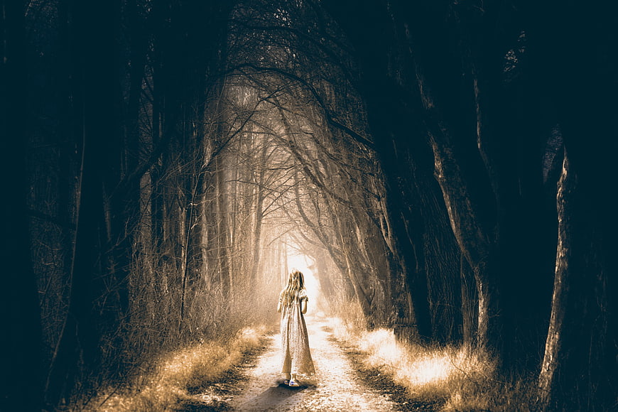 Woman walking down a misty, dark forest path at night