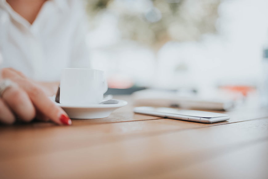 Woman's Hand with Coffee Cup and Smartphone on Wooden Table