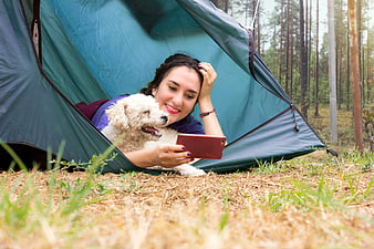 Woman and white dog relaxing in a blue tent in a forest