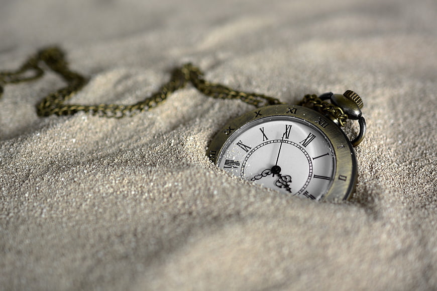 Vintage pocket watch half buried in sand