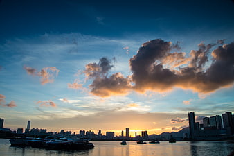 Dramatic Sunset Over City Skyline with Boats on Water