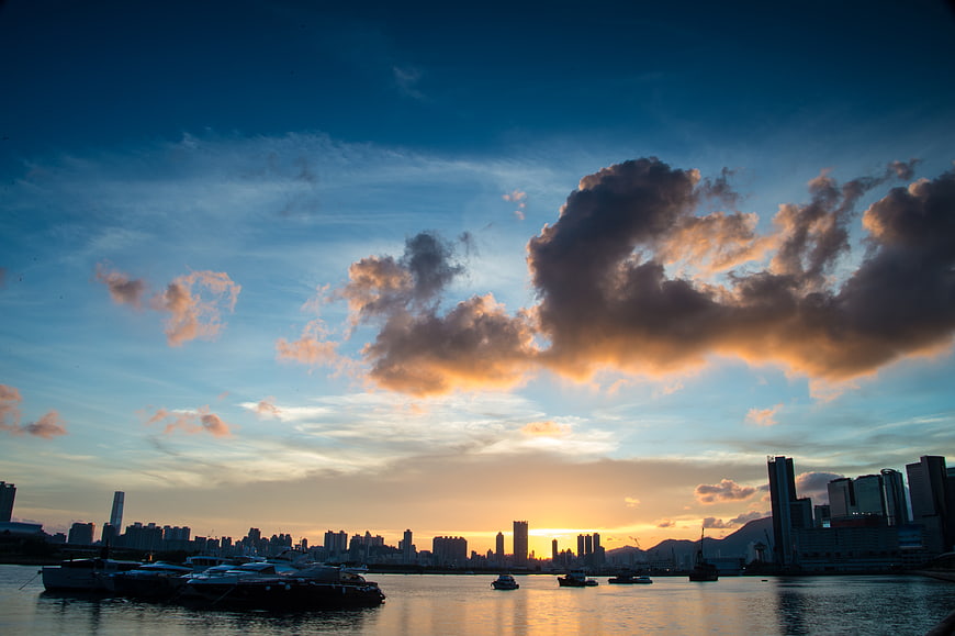 Dramatic Sunset Over City Skyline with Boats on Water