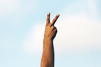 Hand making peace sign against blue sky