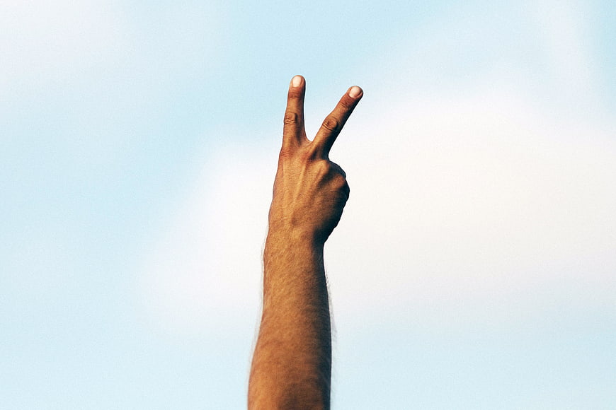 Hand making peace sign against blue sky