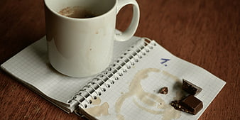 Coffee spill on open grid notebook with chocolate pieces on wooden table