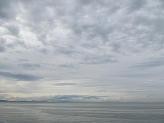 Overcast sky and calm ocean horizon with distant mountains
