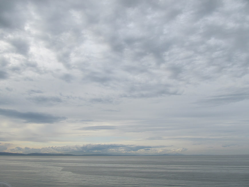 Overcast sky and calm ocean horizon with distant mountains