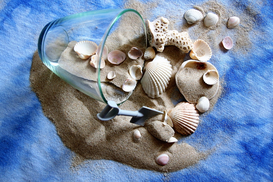 Seashells and sand in glass vase on blue background