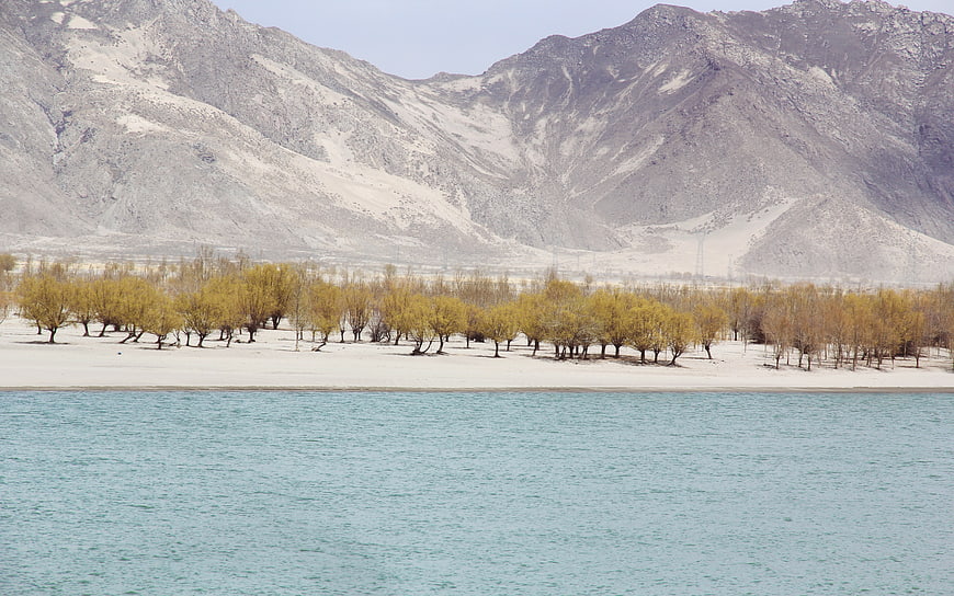 Serene turquoise lake with yellow trees and arid mountains