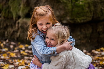 Two happy young girls hugging and laughing in autumn forest