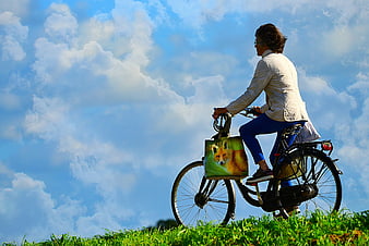 Man Riding Bicycle On Grassy Hill Under Blue Sky