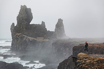 Woman hiking on dramatic volcanic cliffs in foggy coastal landscape