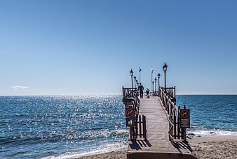 Wooden pier extending into sparkling blue ocean on sunny day