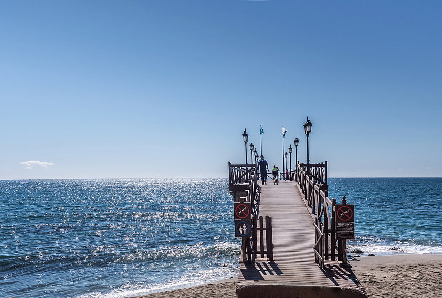 Wooden pier extending into sparkling blue ocean on sunny day