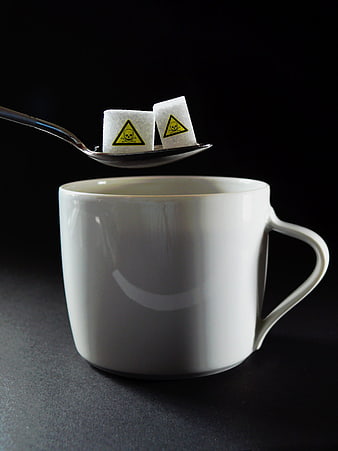 Sugar cubes with poison warning signs on spoon over coffee cup