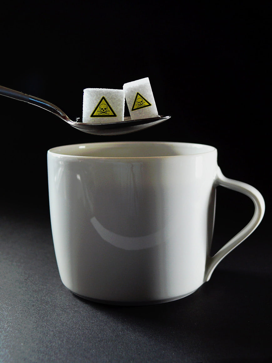 Sugar cubes with poison warning signs on spoon over coffee cup