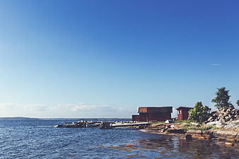 Red Boathouses on Rocky Shoreline with Blue Sky
