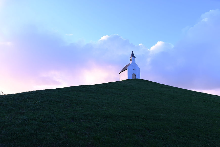 Small white chapel on a green hill against a blue sky