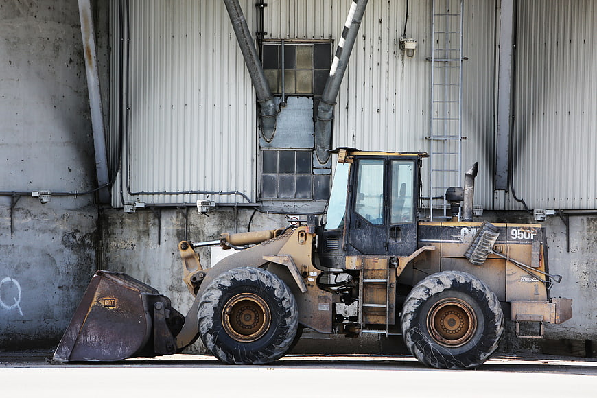 Yellow Caterpillar Wheel Loader Parked Against Industrial Wall