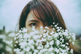 Close-up of woman's eyes peeking through white baby's breath flowers