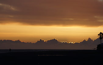 Silhouette of lone figure on beach at sunset with golden clouds