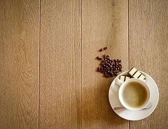 Coffee cup with beans and chocolate on wooden surface