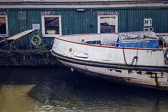 Old white boat docked at green warehouse on canal