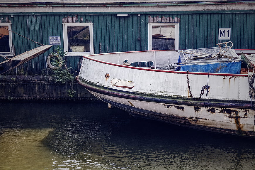 Old white boat docked at green warehouse on canal
