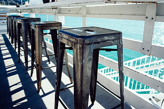 Metal bar stools on a sunny pier overlooking turquoise water