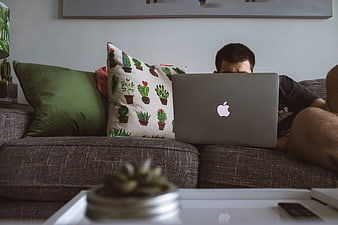Man working on laptop on couch with cactus pillow